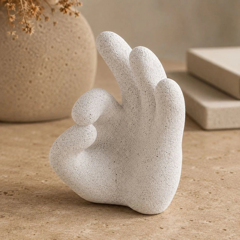 Ballo Hand Sculpture displayed on a dark coffee table, its pale expressive hand form styled among books, ceramics and warm neutral living room furnishings.