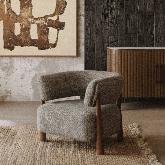 Abigail Ahern Bastian Curved Armchair with a generously cushioned seat, rounded upholstered back and soft neutral fabric, showcasing its elegant vintage-inspired shape in a warm modern living space.
