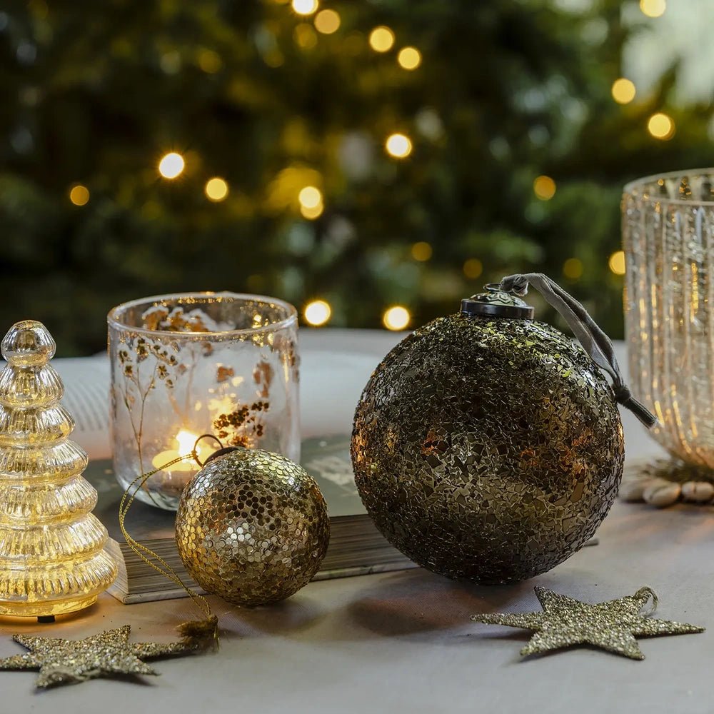 Beau copper flake baubles in contrasting sizes rest on a festive table beside a patterned candleholder, ribbed tree decoration and scattered star ornaments.