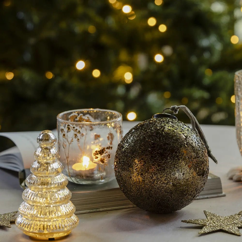 Beau copper flake bauble displays a rounded mottled metallic surface on a festive table beside a smaller bauble, glowing candleholder and ribbed tree lamp.