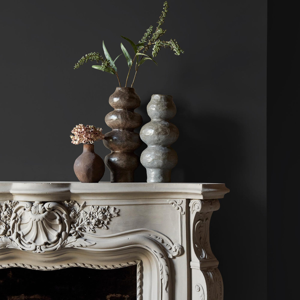 Three ceramic vases sitting on an intricate fireplace mantle in front of a wall in a an anthracite grey paint colour.