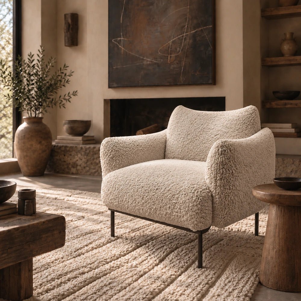 Belville Armchair in soft cream upholstery, styled in a warm interior corner with layered neutral textures, sculptural lighting and contemporary decorative objects.