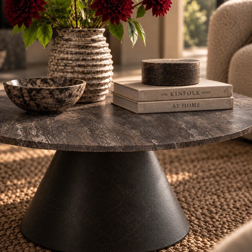 Charcoal Burley Travertine Coffee Table styled with books, textured vase and decorative bowls, showing its dark stone top and sculptural base.
