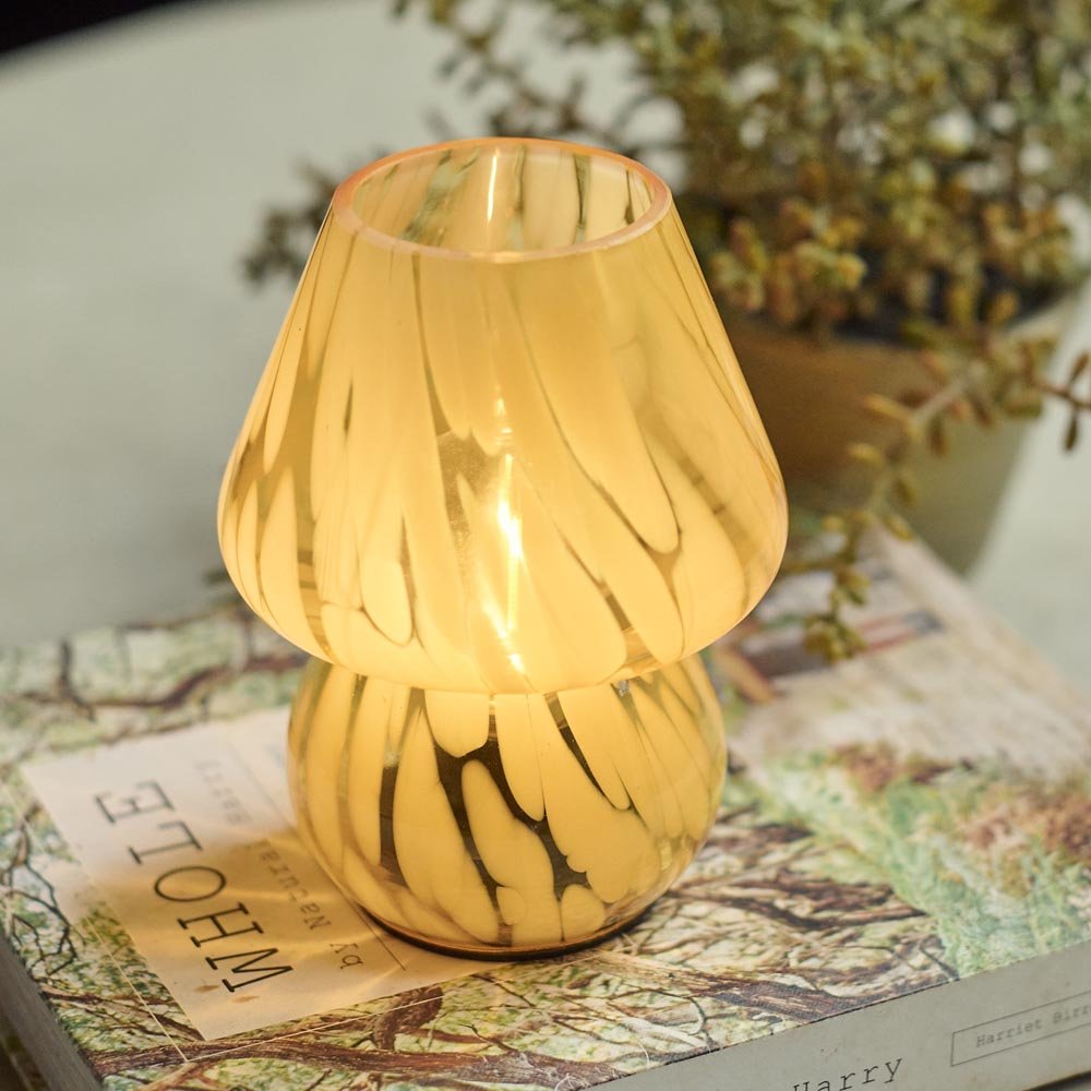 A small battery powered glass table lamp in a subtle lemon colour with a swirly pattern. 
