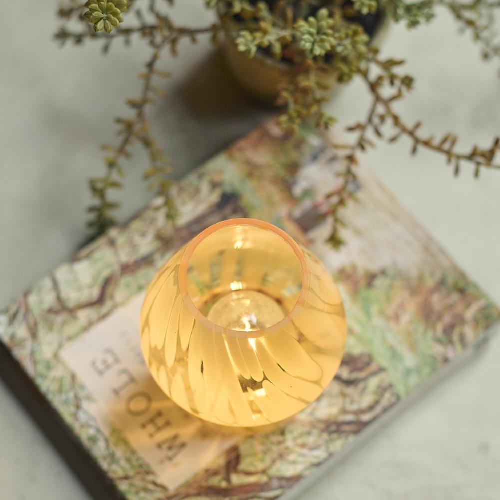 A small battery powered glass table lamp in a subtle lemon colour with a swirly pattern pictured from above.
