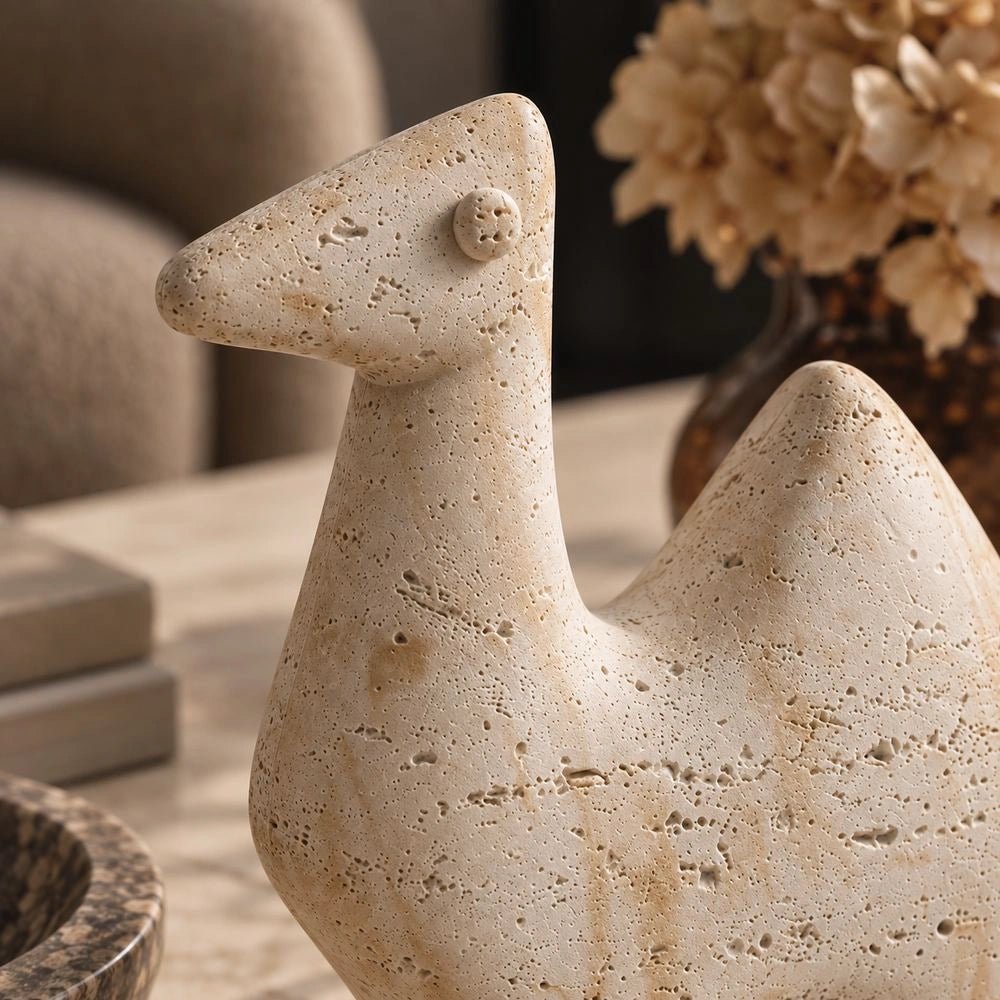 Camel Abstract Sculpture displayed on a dark console table, showing its pale textured animal form beside stacked books, a lamp and sculptural neutral accessories.