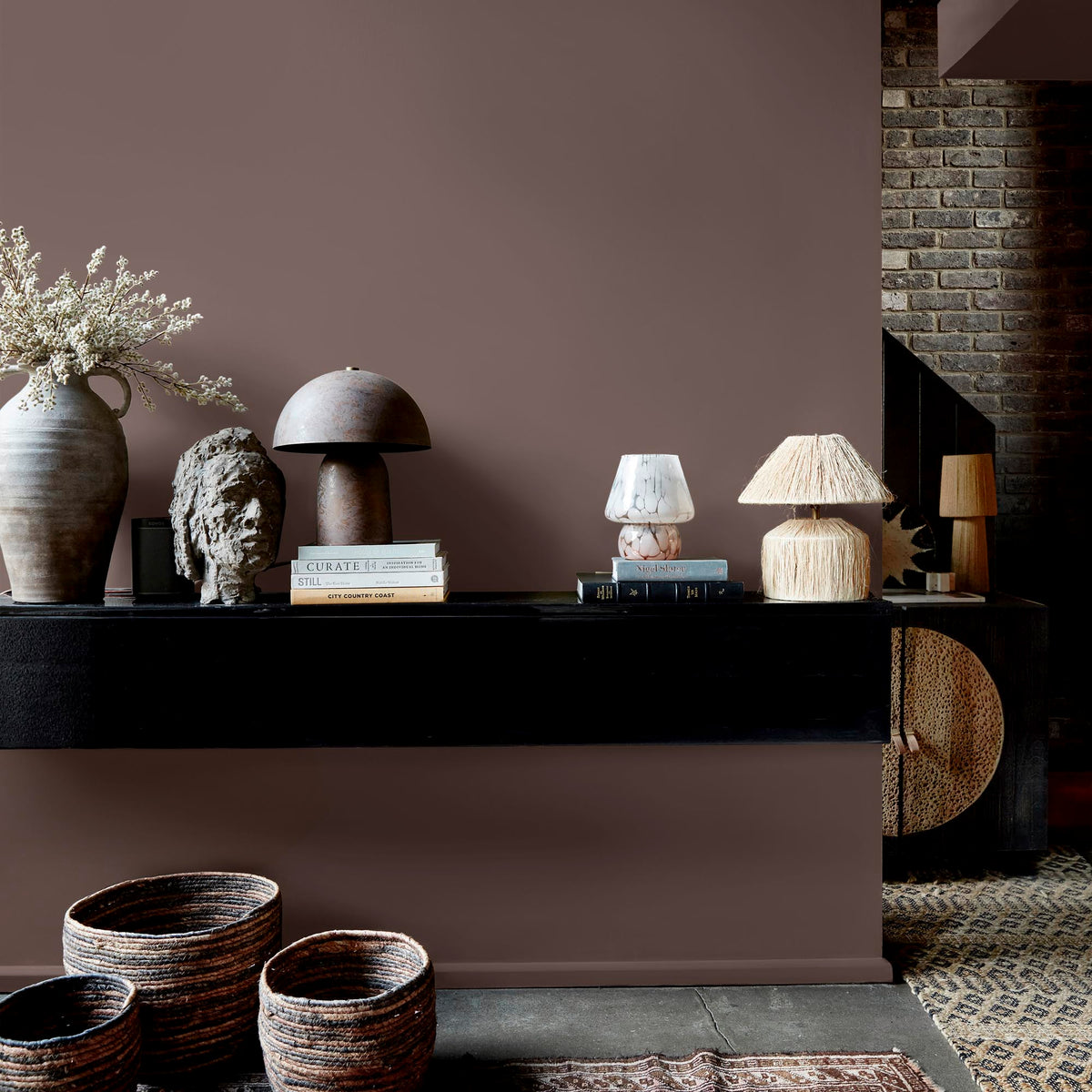 Abigail Ahern Canyon Valley paint – a sumptuous dusky brown with deep plum undertones enveloping a beautifully styled wall with mounted shelf, lamps and vases