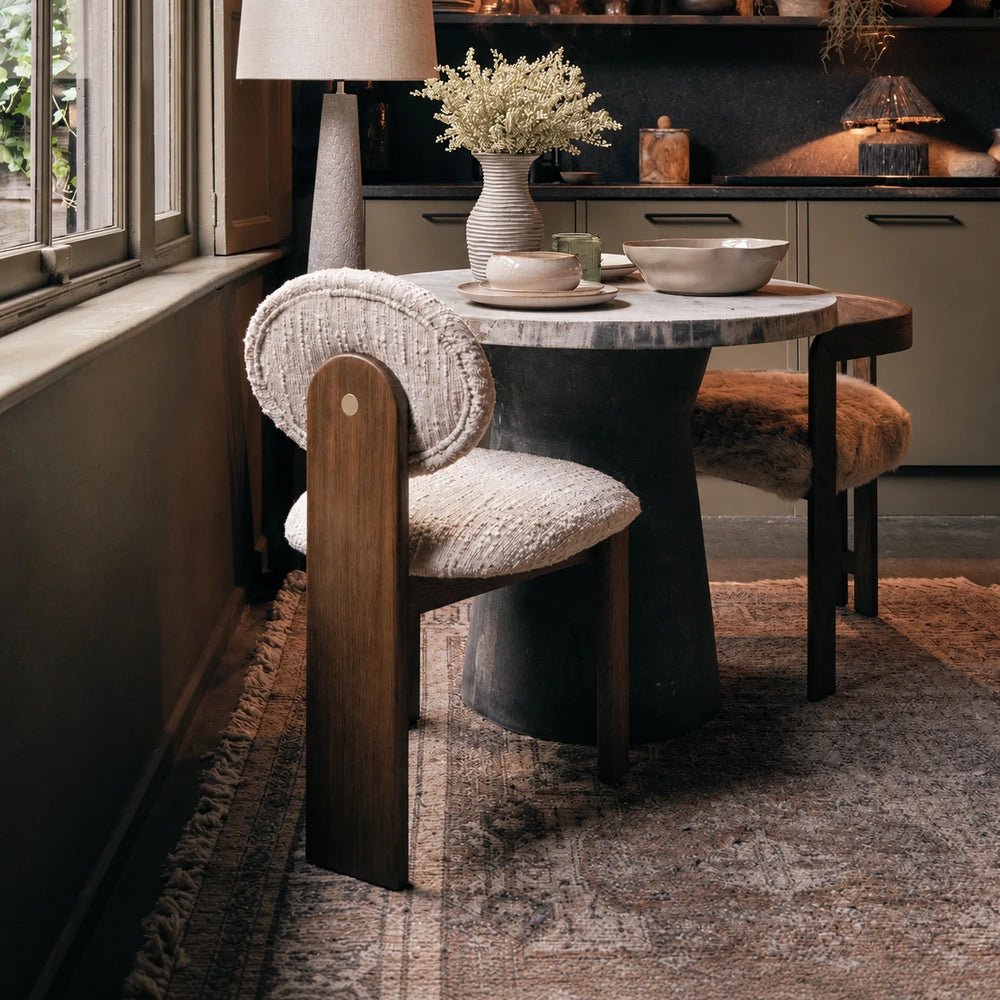 Channing boucle dining chair with cream textured upholstery, a rounded back and warm wooden frame sits beside a round table in a softly lit dining room.