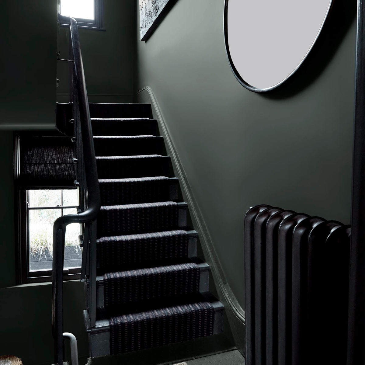 A staircase landing with a large circular mirror and walls painted in an earthy grey paint colour with green and blue undertones.