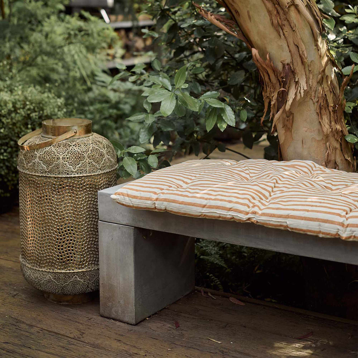 The Daltona Mattress, a slim rectangular mattress in warm ochre and sand coloured stripes, on a concrete bench on a patio.