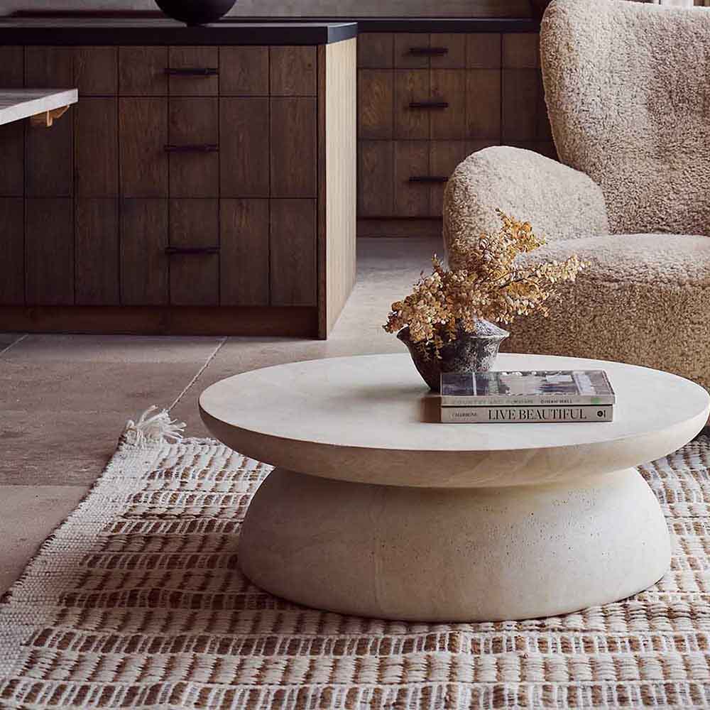 Round travertine effect coffee table with a soft beige finish, subtle cream and grey tones and a sculptural contemporary design. Diablo Round Coffee Table by Abigail Ahern, crafted from glass-reinforced concrete with a textured stone-inspired surface and suitable for both indoor and outdoor spaces. A luxury statement coffee table perfect for modern living rooms and stylish interiors, adding natural texture, timeless elegance and a refined focal point to your home decor.