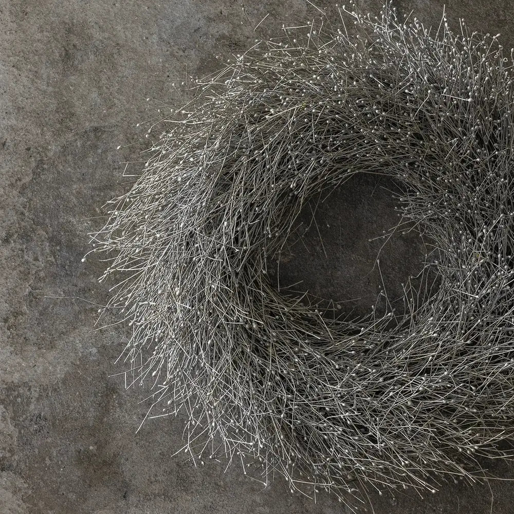 Dried gypsophilia wreath displays a dense ring of fine grey branches and tiny pale buds, hanging against a mottled wall with an open circular centre.