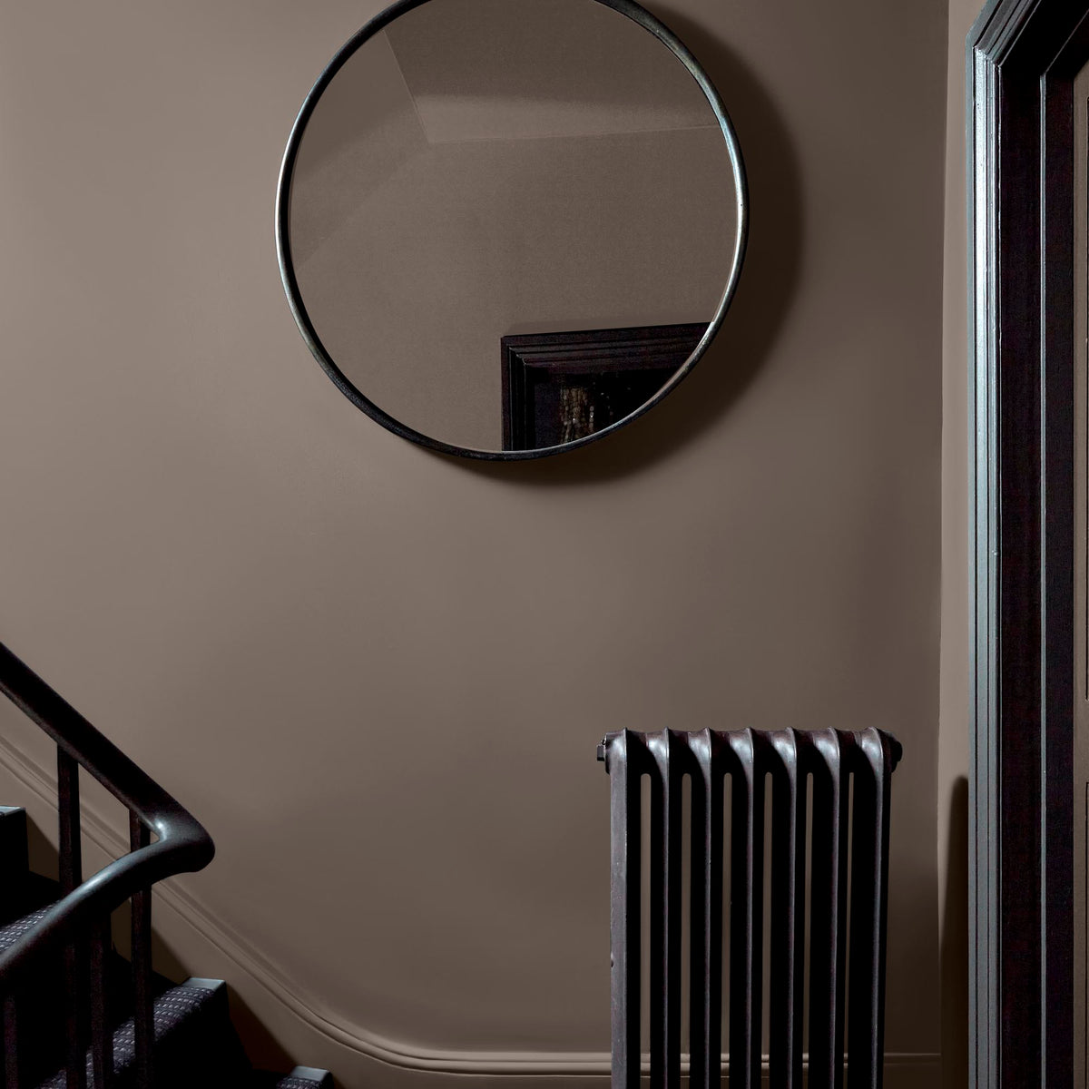 Abigail Ahern Dusk Falls paint – a sumptuous deep beige with warm undertones enveloping a staircase landing styled with a large circular mirror