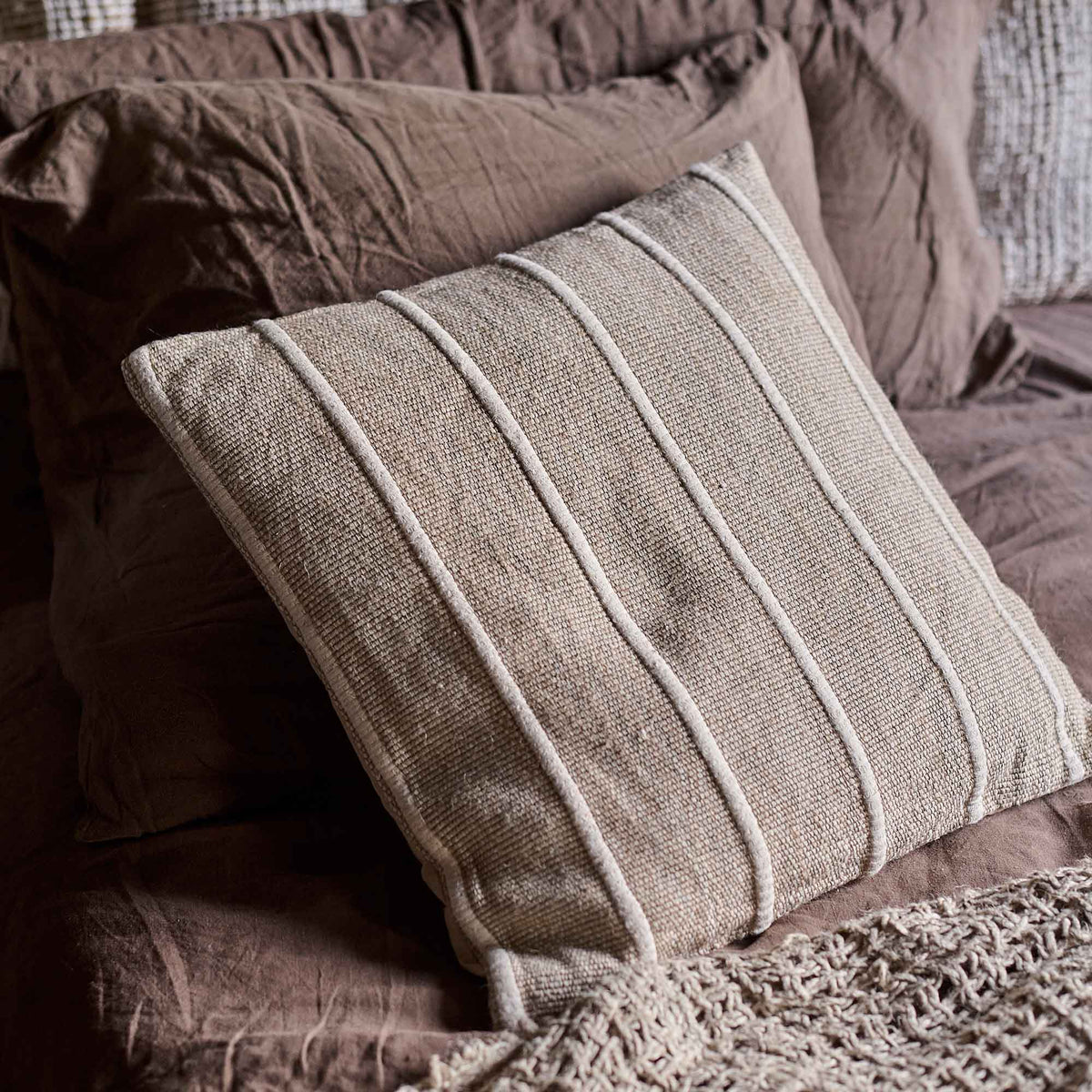 A closeup of the Edwina Striped Cushion against some warm brown linen pillows.