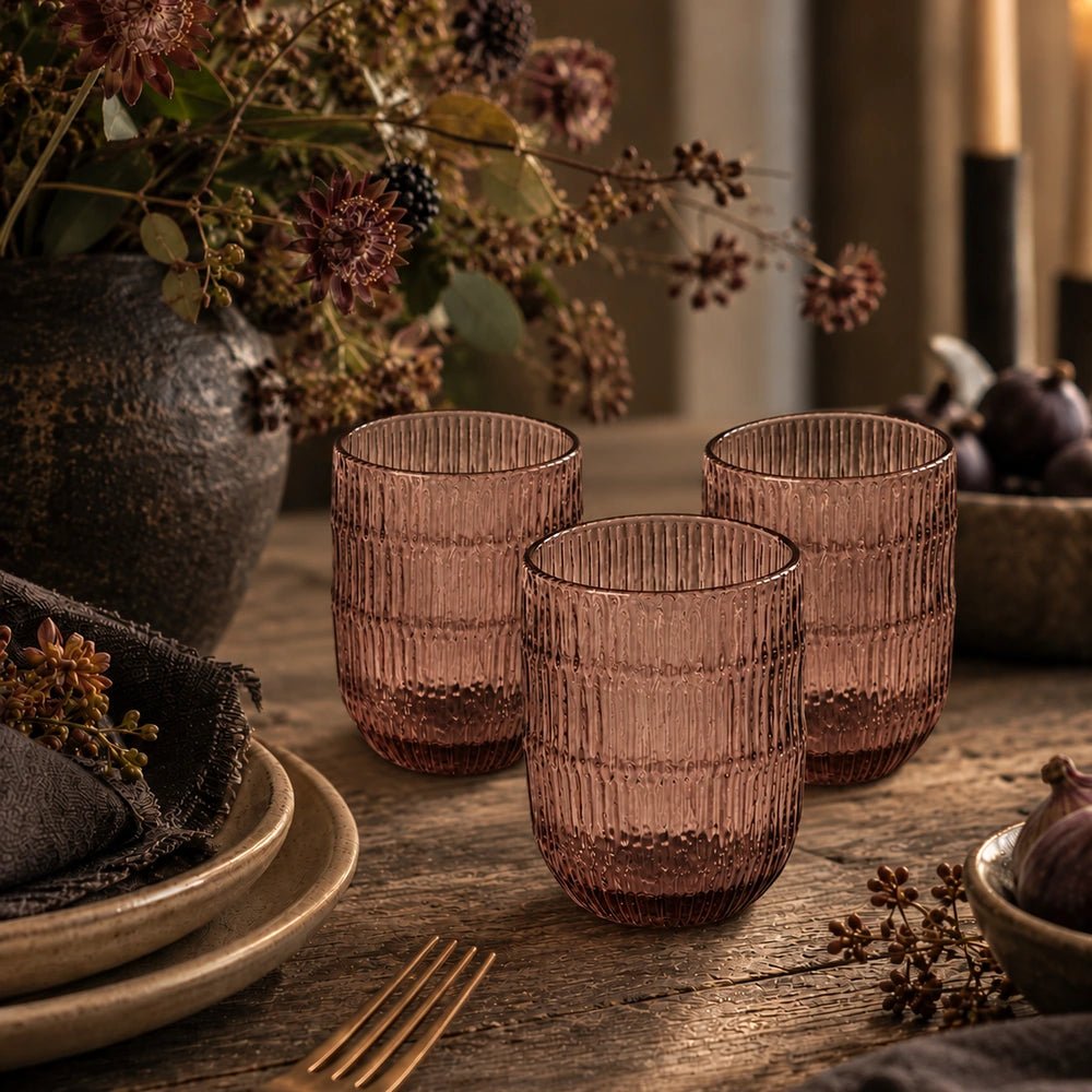 Elden Glass Cup, Blush set of three ribbed translucent tumblers styled on a rustic dining table beside dark florals, ceramic plates and warm candlelight.