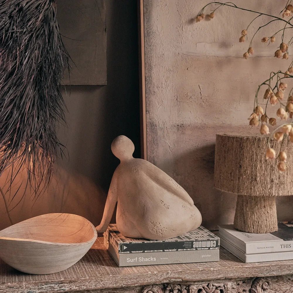 Ellery Figurative Sculpture shows the curved back of a seated figure, styled on books beside a textured lamp against a warm neutral wall.
