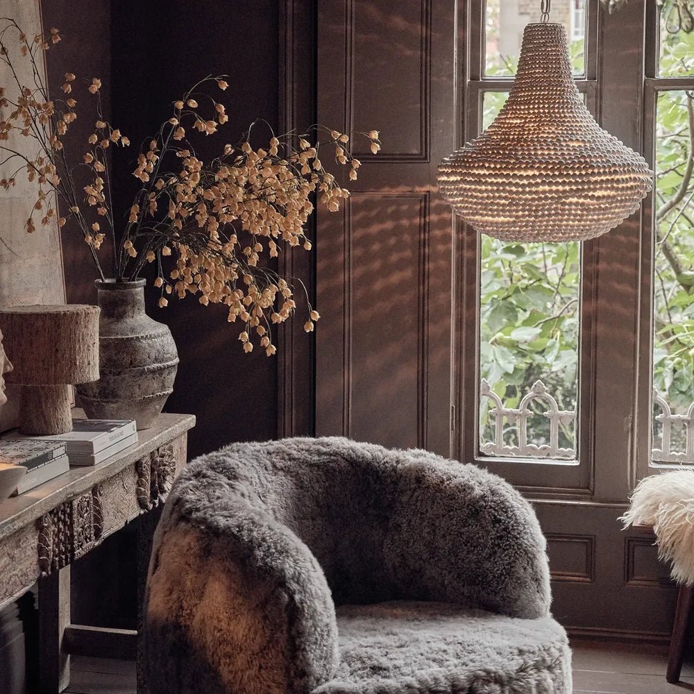 Eloise Beaded Chandelier hangs beside a tall window above a textured armchair, with pale beads complementing the room’s dark walls and natural accents.