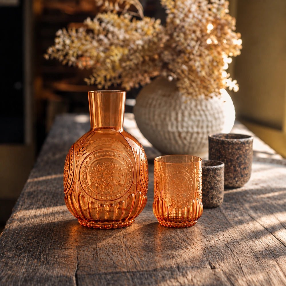 Ember Carafe and Cup Set in warm amber glass, arranged on a sunlit table beside textured ceramics and dried flowers in a relaxed dining setting.