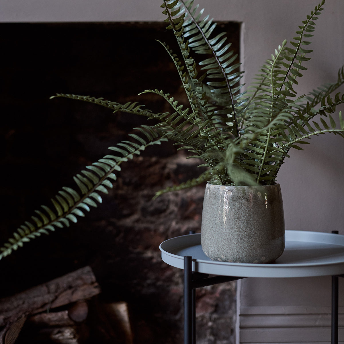 The Artificial Fern in Khaki Pot, a tall faux potted fern in a glossy khaki coloured glazed ceramic pot on a side table. 