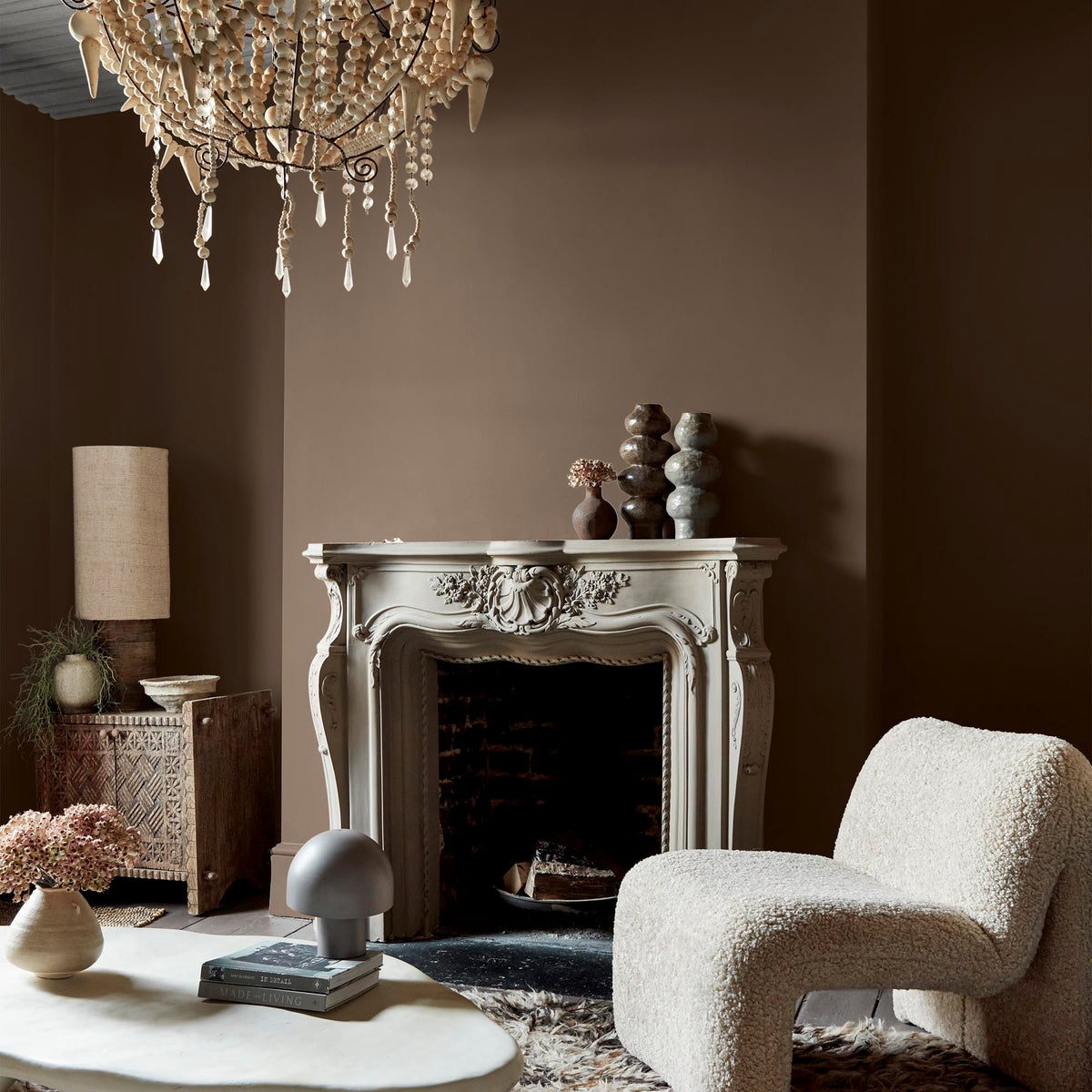 A coffee table and accent chair sitting in front of a fireplace, with the walls painted a soft brown paint colour.