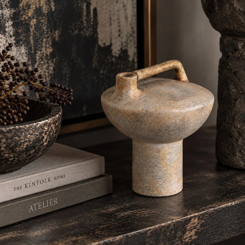 Forbes sand ceramic vase with a textured beige finish, broad rounded body and raised rectangular handle stands beside stacked books and a bowl on a console.
