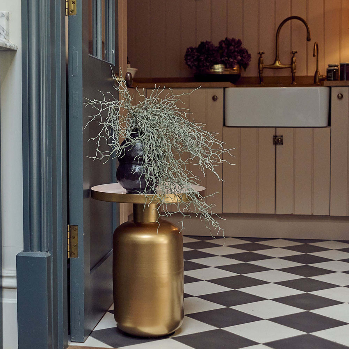 The Giles Gold Side Table, a round table with a wide curved cylindrical base in gold effetc and a white enamel tray style top.