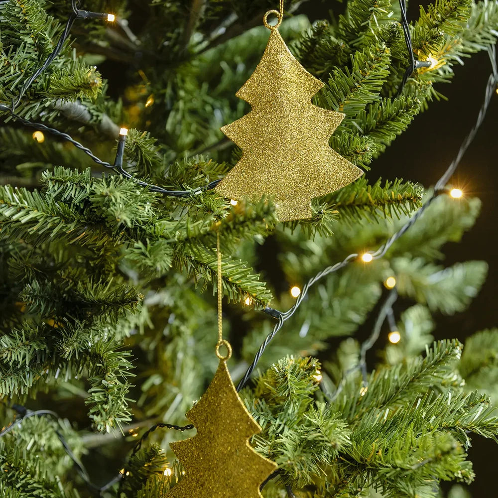 Glittering tree baubles display layered gold tree silhouettes among green branches, with hanging loops and sparkling surfaces illuminated by small warm Christmas lights.