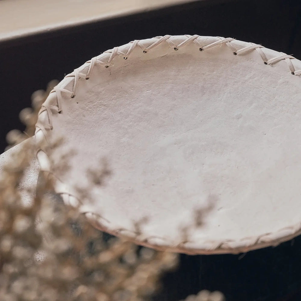 Halstead paper mache decorative bowl shown beside blurred dried flowers, with its wide shallow interior, off white textured finish and cord lacing around the rim.