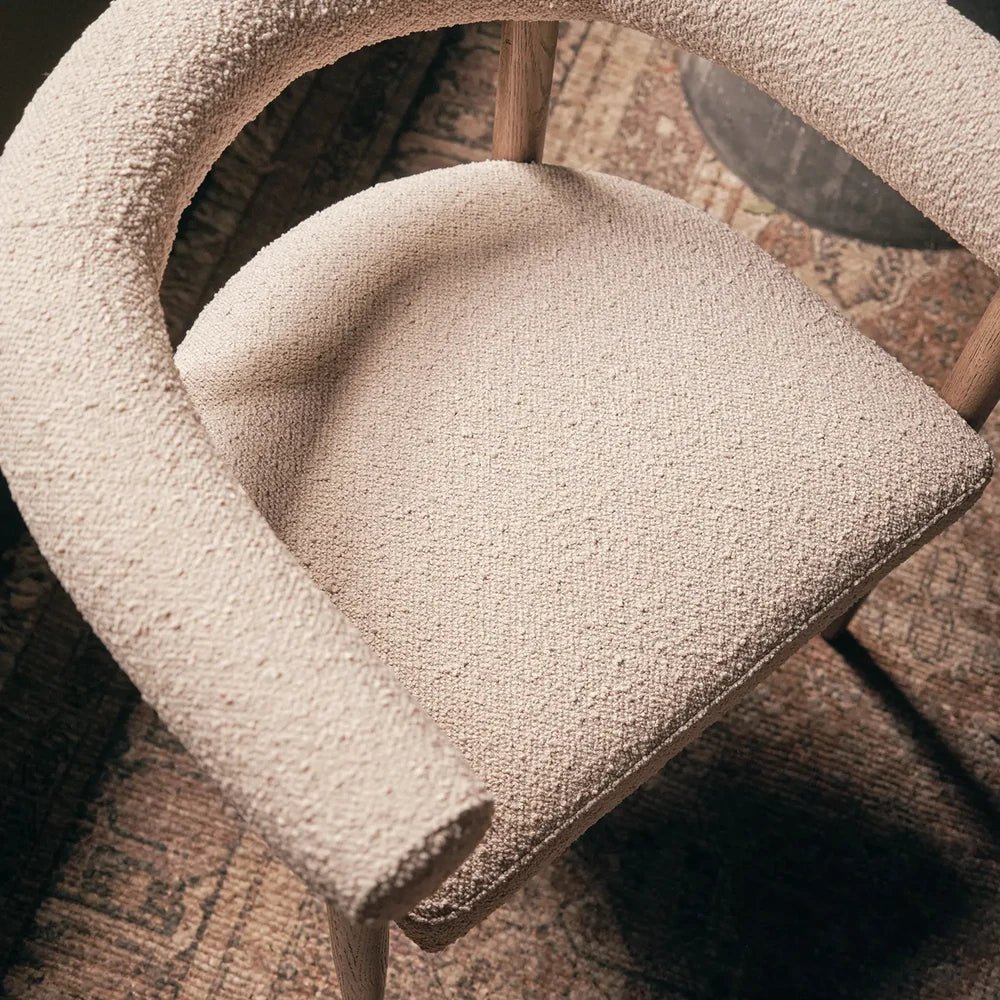Harrington Boucle Dining Chair detail shows a padded cream seat and curved open back, with textured upholstery and wooden legs against a patterned rug.