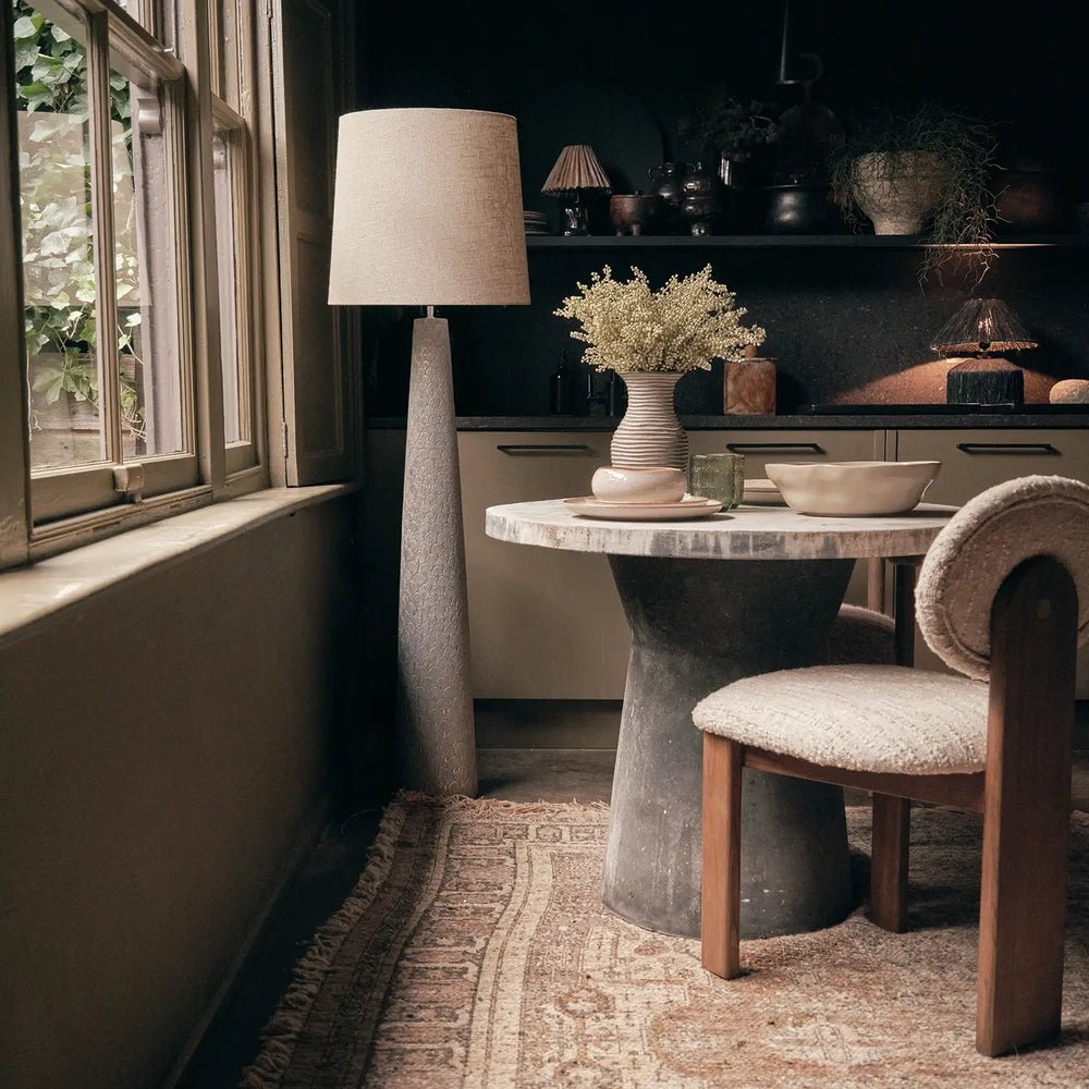 Haverford Polyresin Floor Lamp stands beside a dining table near a window, combining a pale tapered shade with a tall sculpted neutral base.