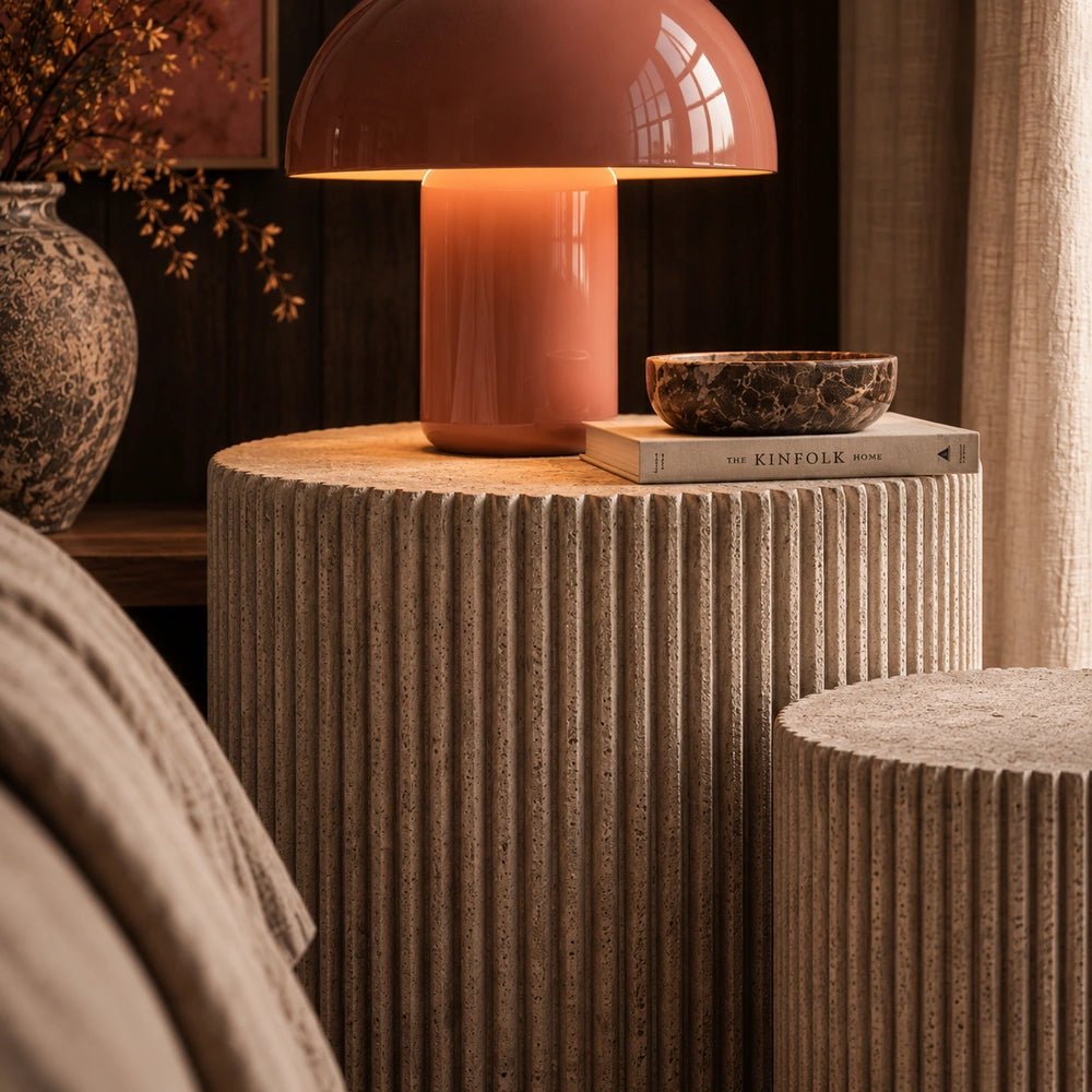 Textured Hereford stone side table with vertical fluted surface, styled beside a warm orange table lamp and decorative bowl in a softly lit interior.