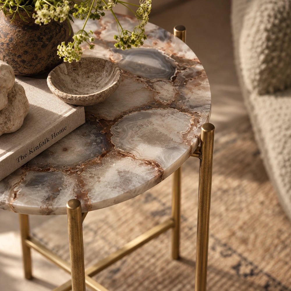 Angled close-up of the Hexton Agate Side Table highlighting its patterned circular stone top and slim brass-toned legs, styled with books and decorative bowls.