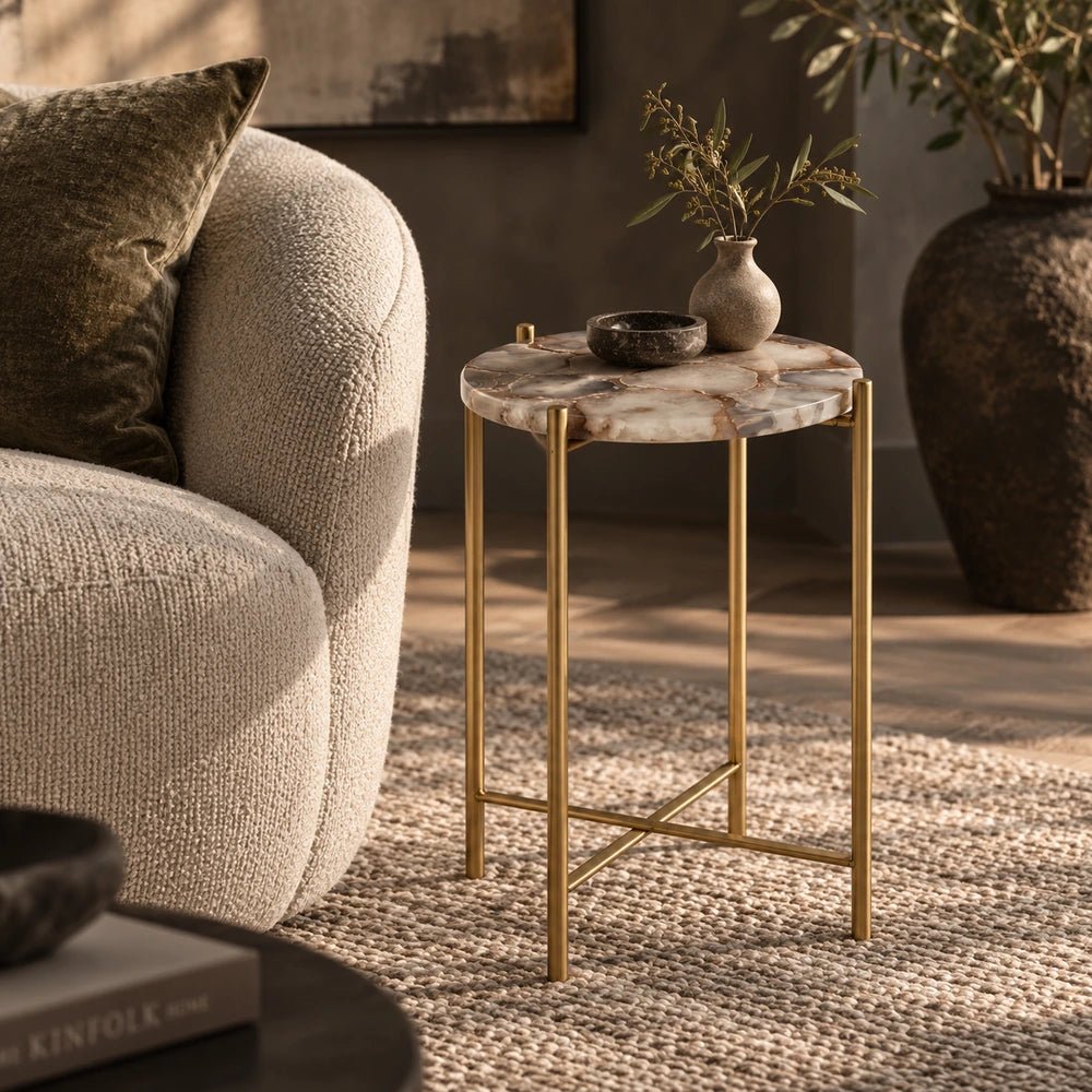Hexton Agate Side Table with round stone top and slim brass-toned frame, styled beside a curved cream armchair in a warm neutral living room.