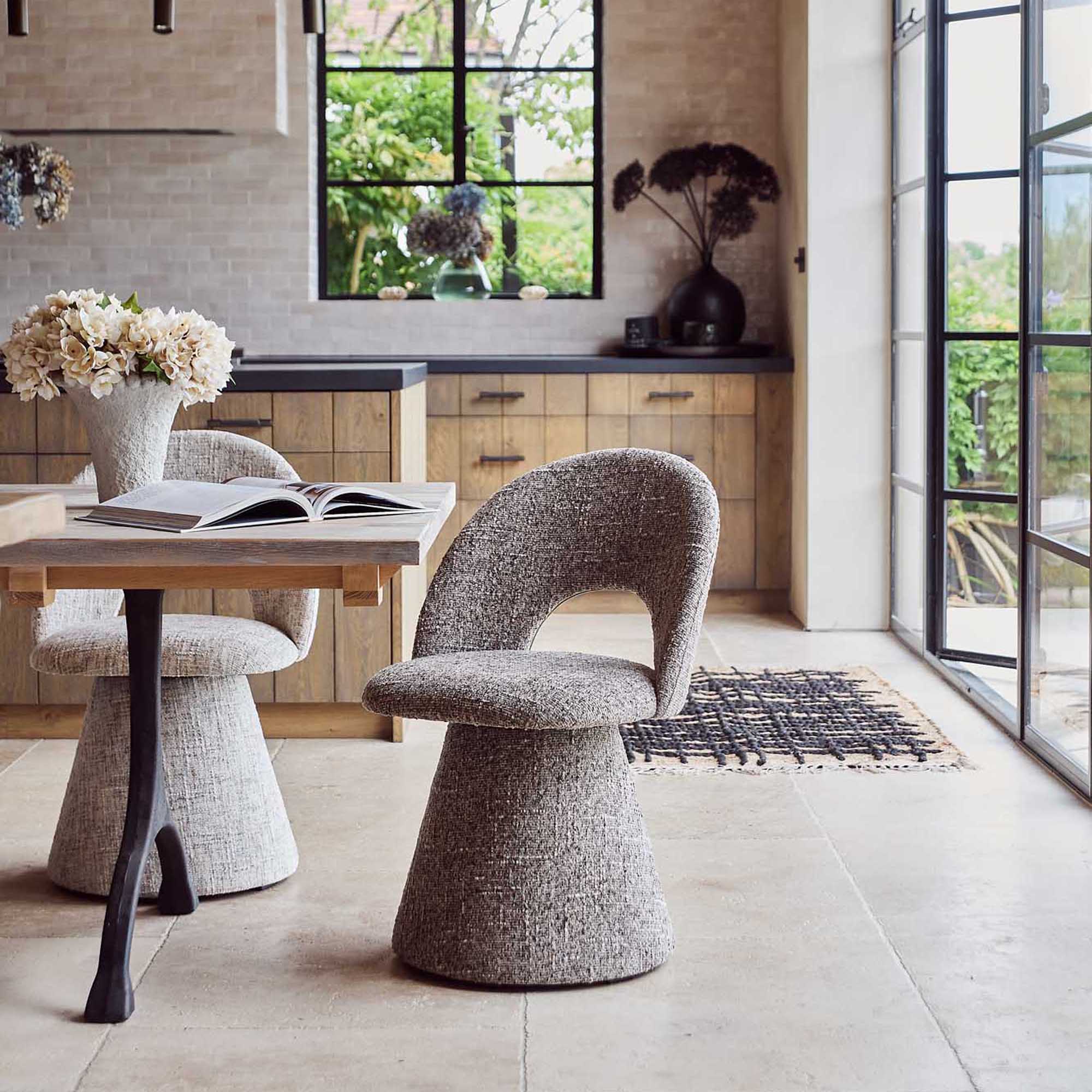 Contemporary upholstered, comfortable dining chair in a textured light brown grey fabric featuring a sculptural curved silhouette a modern but organic design for stylish dining interiors.