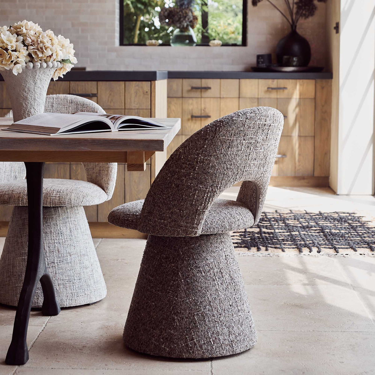 Contemporary upholstered, comfortable dining chair in a textured grey fabric featuring a sculptural curved silhouette a modern but organic design for stylish dining interiors.