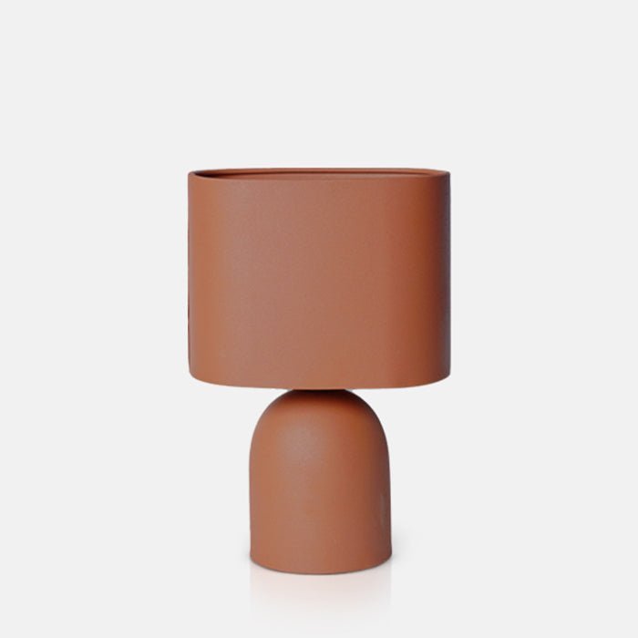 Cutout image on a white background of a terracotta coloured table lamp. This modern table lamp has a cylindrical base and a matching shade.