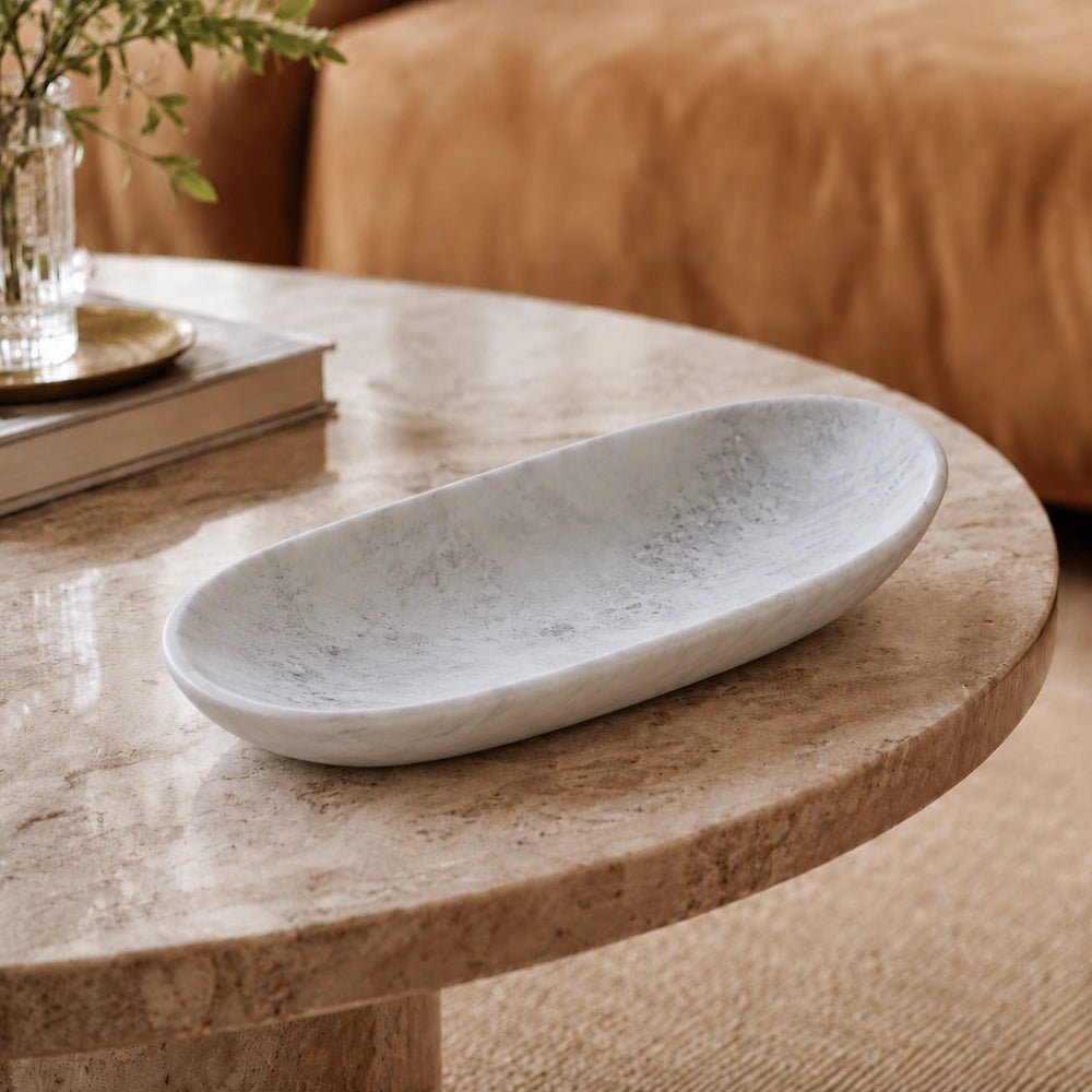Irwin Resin Dish in soft white with a long oval shape and subtle marbled texture, styled on a round stone table in a warm living room.