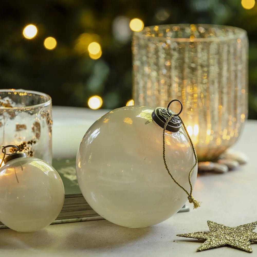 Kendal large opal bauble with a round pearl white surface and hanging loop sits beside a smaller ornament and glowing candleholders on a festive table.