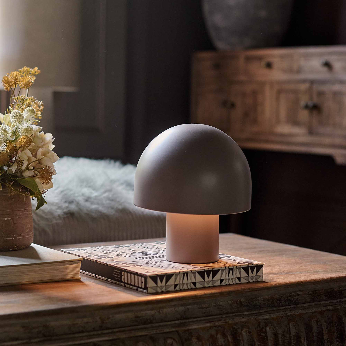 A small portable grey table lamp in a mushroom shape with a smooth metal finish styled on a coffee table. 