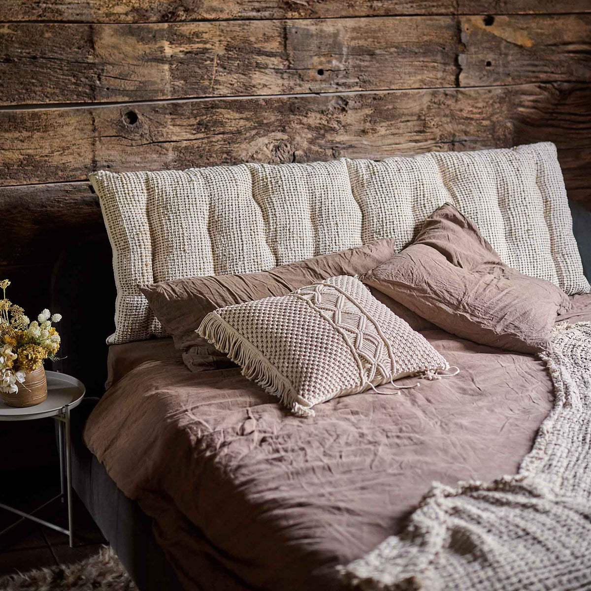 The Konta Headboard Cushion, a long rectangular sumptuous padded cushion in woven jute and cushion, on a cosy bed.