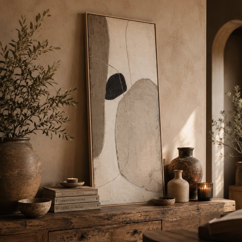 Levity Painting displayed above a dark sofa, featuring layered abstract neutral shapes in a warm living room with textured cushions and sculptural lighting.