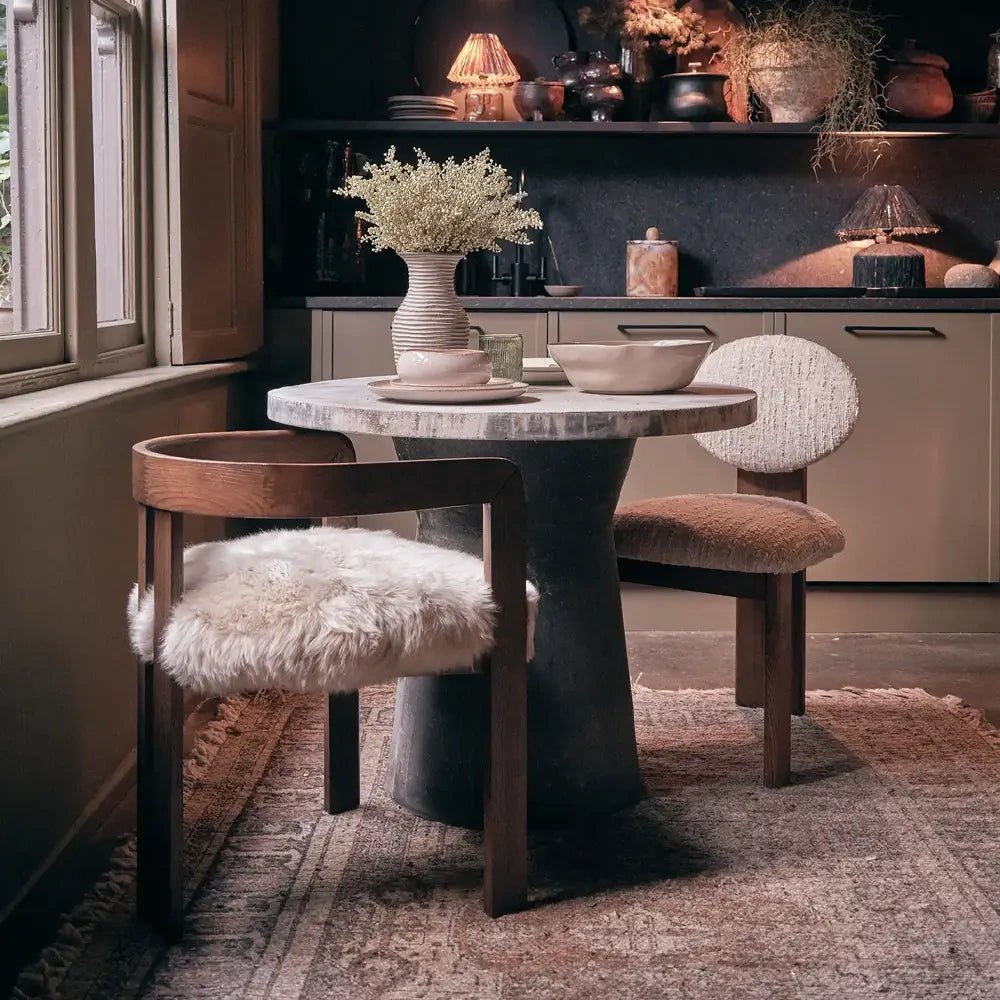 Loxford Sheepskin Dining Chair combines a curved wooden frame with a pale fluffy seat, shown beside a round table in a softly lit dining room.