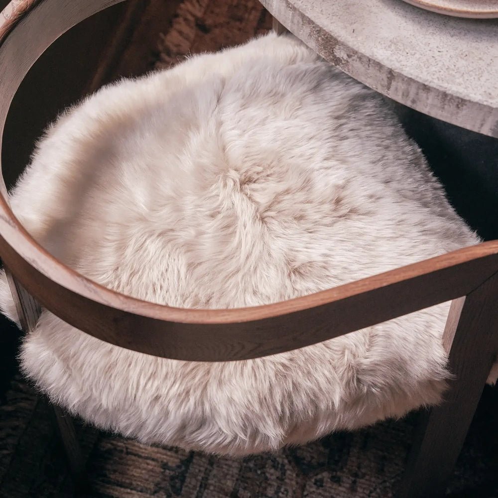 Loxford Sheepskin Dining Chair reveals its pale fluffy seat and smooth curved wooden frame in a close-up view beside the edge of a dining table.