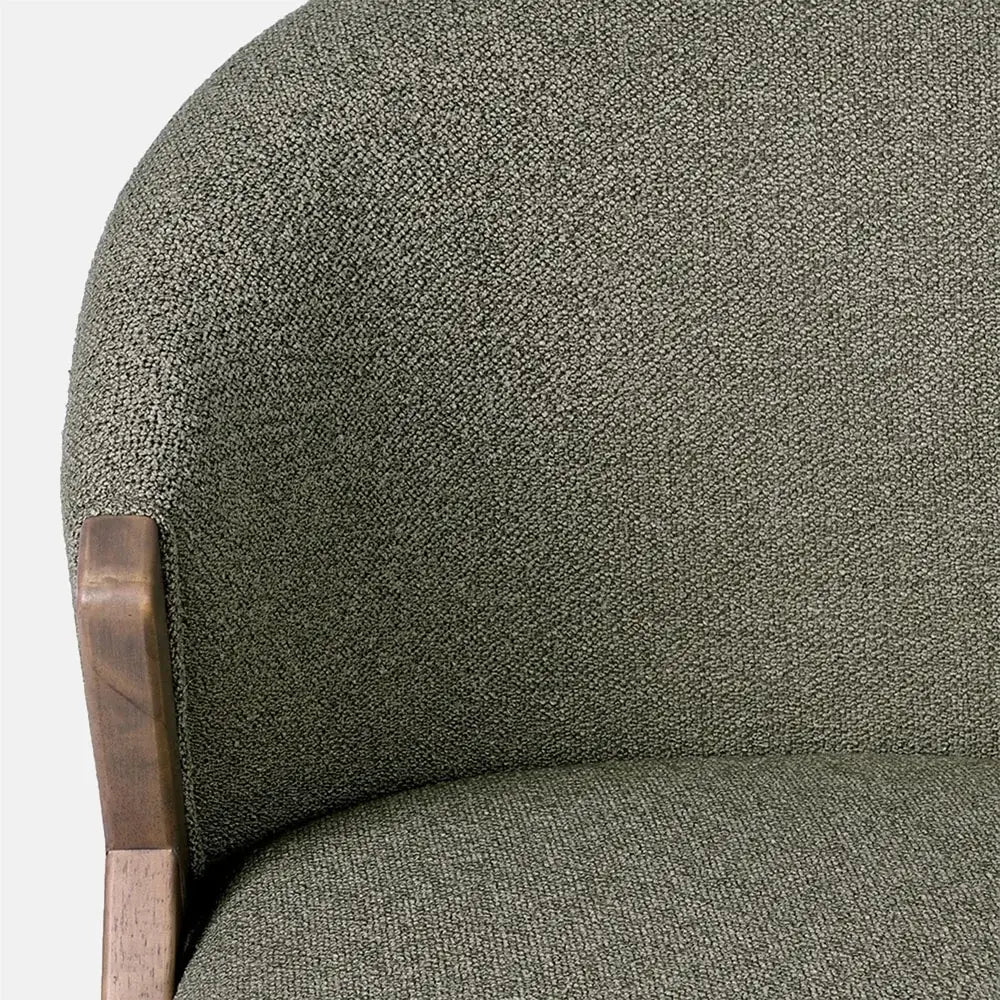 Lyndon Curved Accent Chair in pistachio features a rounded upholstered back with a fine green woven texture, framed by warm wooden supports beside the seat.