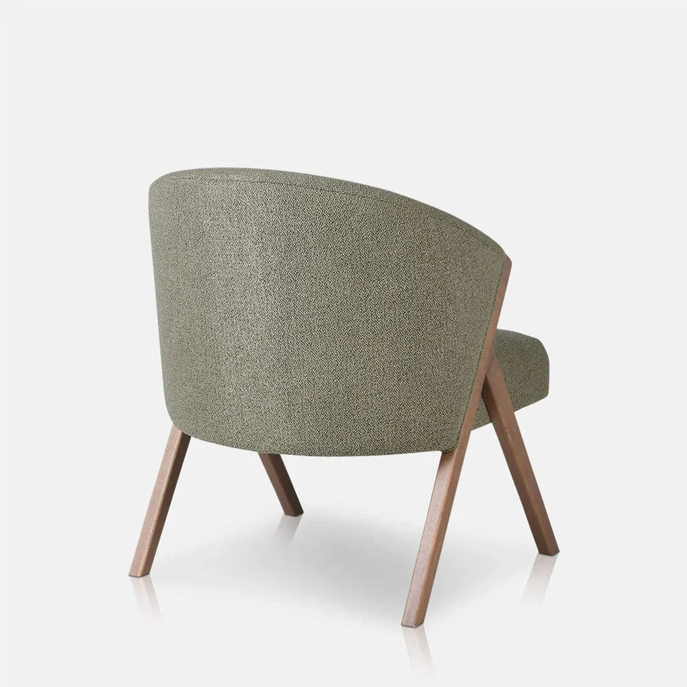 Lyndon Curved Accent Chair in pistachio shows its rounded green upholstered back from behind, with a warm wooden frame and splayed legs supporting the seat.