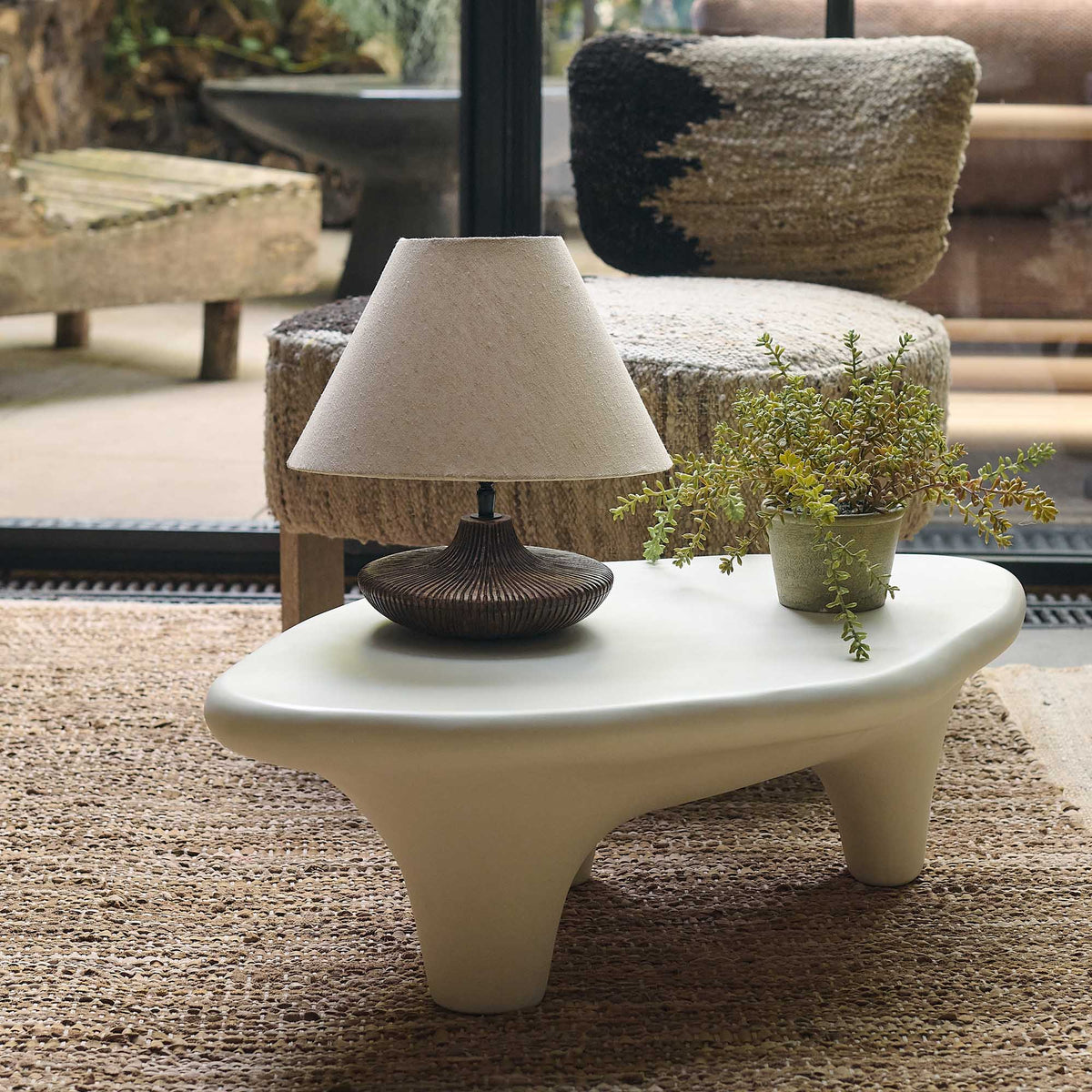 medium sized cream sculptural coffee table with organic rounded silhouette and chunky legs, styled on natural jute rug with table lamp and potted plant, rounded edges, contemporary living room Cream stone effect coffee table with a sculptural round design, curved silhouette and textured organic finish. Medina Coffee Table by Abigail Ahern, featuring a contemporary shape and neutral tones that create an elegant centrepiece for modern living rooms and luxury interiors. A statement designer coffee table perf

