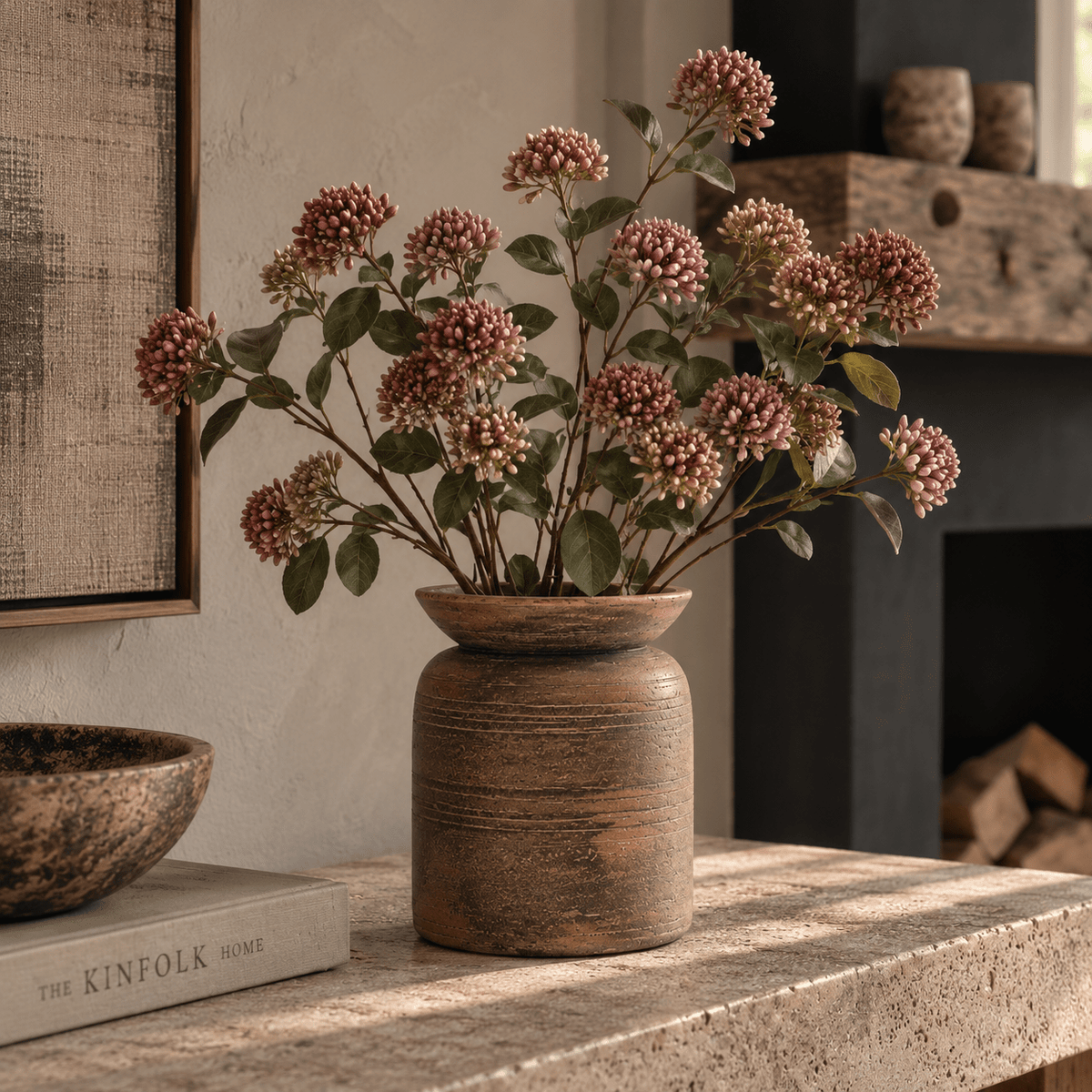 Massin Vase Medium in rich earthy brown ceramic, styled with leafy stems on a warm wooden console alongside sculptural neutral decorative accessories.