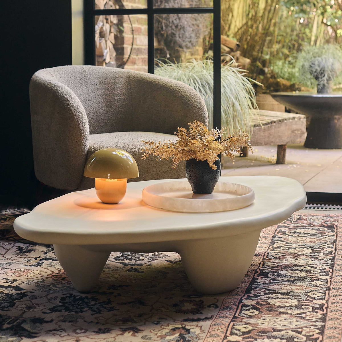 Cream stone effect coffee table with a sculptural round design, curved silhouette and textured organic finish. Medina Coffee Table by Abigail Ahern, featuring a contemporary shape and neutral tones that create an elegant centrepiece for modern living rooms and luxury interiors. A statement designer coffee table perfect for styling with decorative accessories, books and lighting, adding natural texture and timeless sophistication to your home decor.