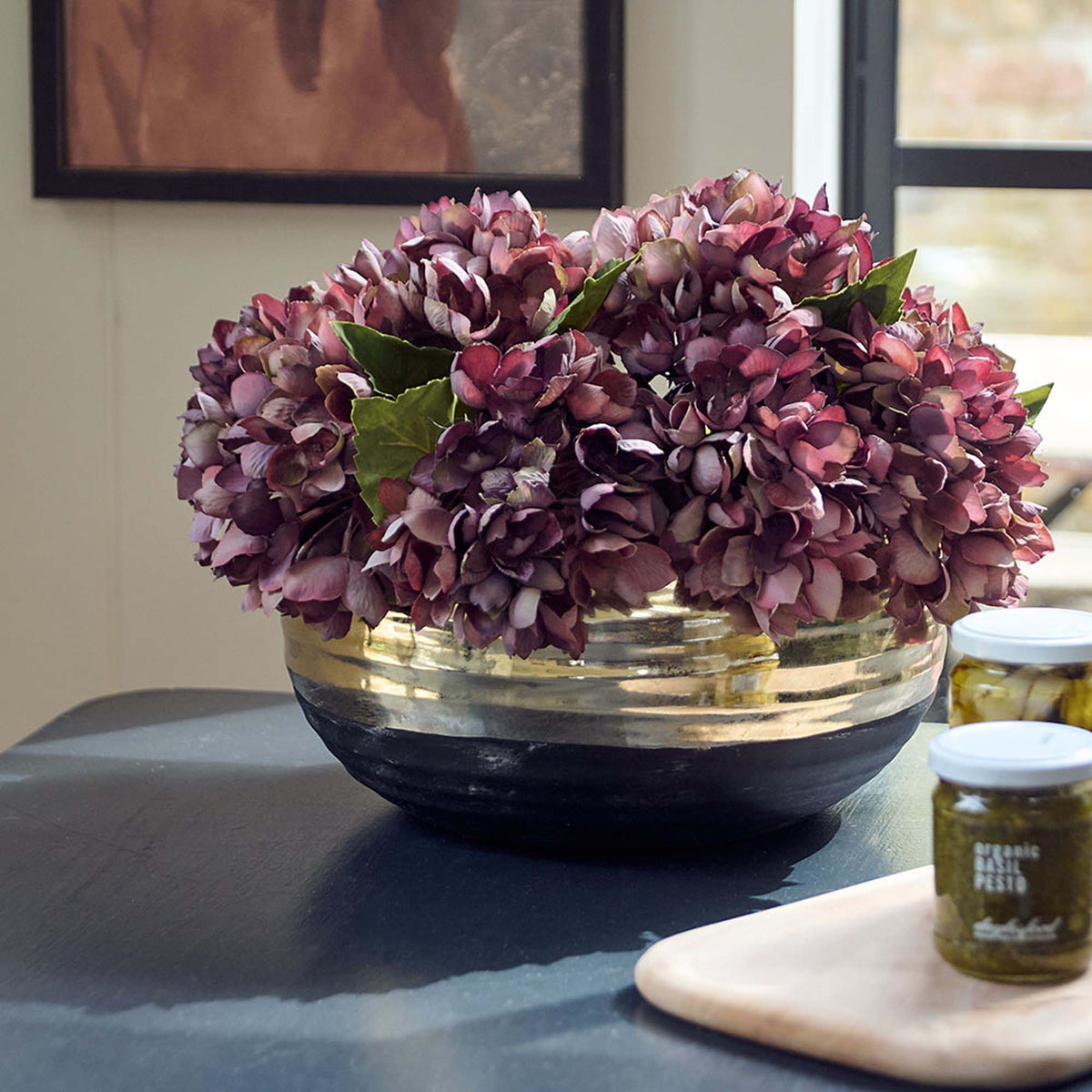 Merritt Stone Decorative Bowl, a sleek wide low black bowl with a wide gold band around the top, holding damson hydrangeas.