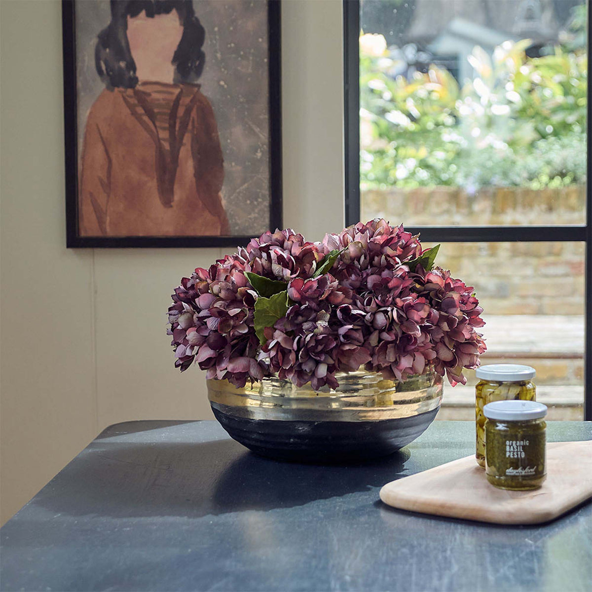 Merritt Stone Decorative Bowl, a sleek wide low black bowl with a wide gold band around the top, holding damson hydrangeas.